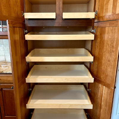 home-hero-vertical-sized.jpeg – Roll 'em Out Shelves A tall wooden pantry cabinet with both doors open, revealing six pull-out shelves. The shelves are empty and extend outward, showing light wood interiors and smooth drawer slides.